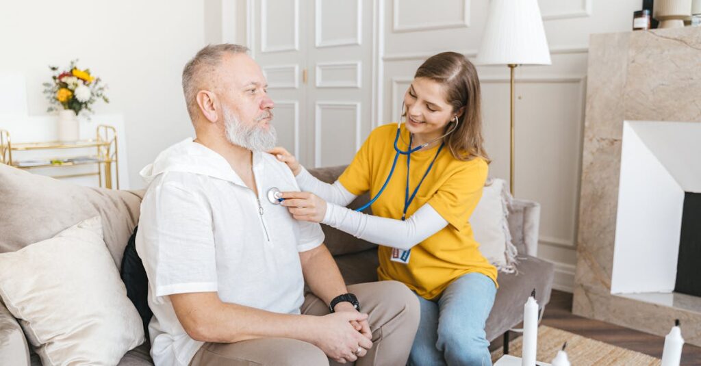 A nurse uses a stethoscope for a home check-up on a senior adult in a cozy living room.